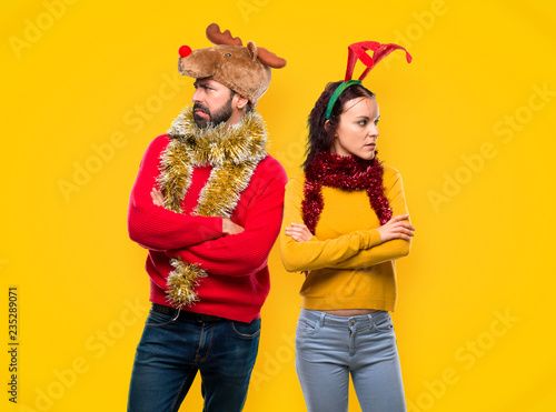 Couple dressed up for the christmas holidays having doubts and with confuse face expression while bites lip on yellow background