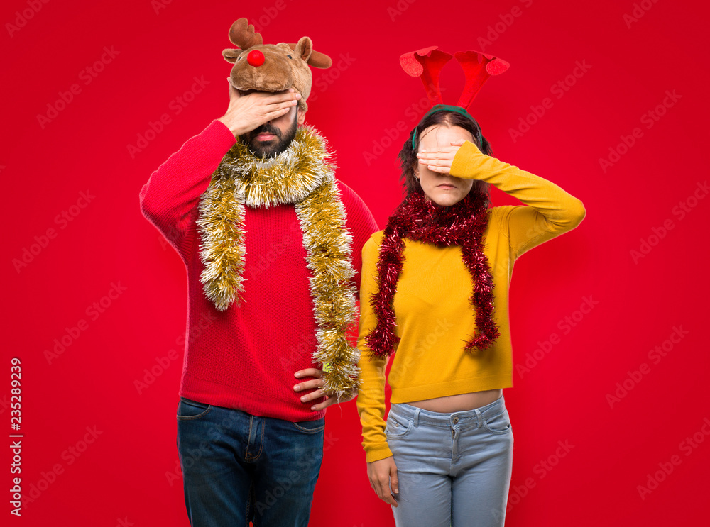 Couple dressed up for the christmas holidays covering eyes by hands. Do not want to see something on isolated red background