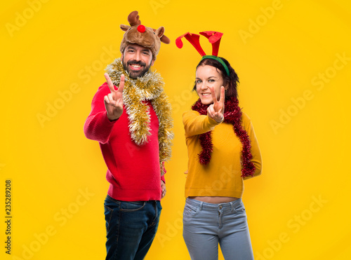 Couple dressed up for the christmas holidays smiling and showing victory sign on yellow background