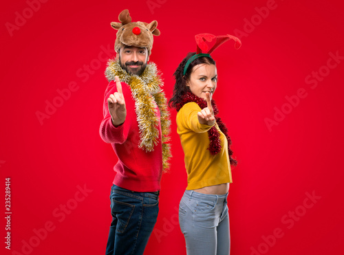 Couple dressed up for the christmas holidays showing and lifting a finger in sign of the best on isolated red background