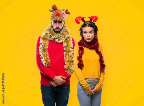 Couple dressed up for the christmas holidays with sad and depressed expression. Serious gesture on yellow background