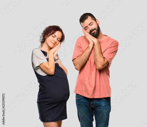 Couple with pregnant woman making sleep gesture. Adorable sweet expression on isolated grey background