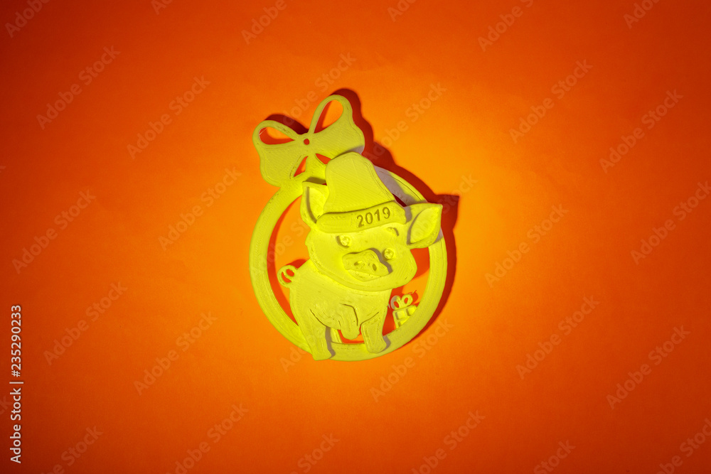 Cheerful yellow pig, in a cap with the inscription 2019, a symbol of the New Year, a toy on the Christmas tree, made of plastic on a 3D printer at home, on a red background Cheerful yellow pig, in a cap with the inscription 2019, a symbol of the New Year, a toy on the Christmas tree, made of plastic on a 3D printer at home, on a red background