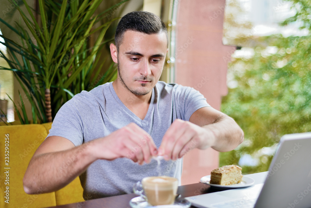breakfast young guy in cafe pours sugar in cup of cappuccino coffee breakfast young guy in cafe pours sugar in cup of cappuccino coffee