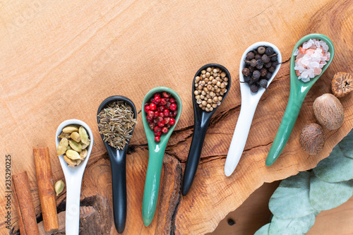 Exotic herbal Food concept Mix of the organic Spices cinnamon stick, cardamom pods, cumin, black pepper, pink peppercorn, nutgeg and coriander seeds in white ceramic spoon on a wood background photo