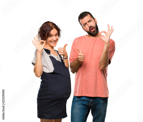 Couple with pregnant woman showing ok sign and giving a thumb up gesture with the other hand on isolated white background