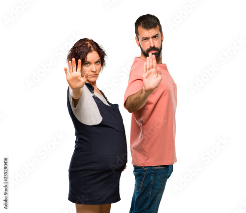 Couple with pregnant woman making stop gesture with her hand denying a situation that thinks wrong on isolated white background