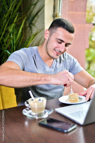 young guy is freelancer in cafe working behind a laptop. man drinking coffee