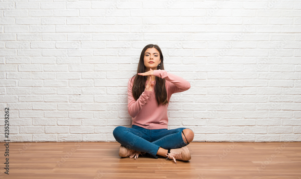 Teenager girl sitting on the floor in a room making stop gesture with her hand to stop an act Teenager girl sitting on the floor in a room making stop gesture with her hand to stop an act