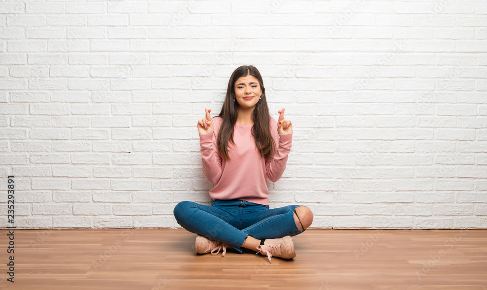 Teenager girl sitting on the floor in a room with fingers crossing and wishing the best
