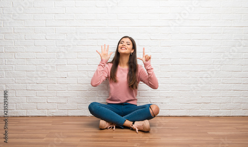 Teenager girl sitting on the floor in a room counting seven with fingers