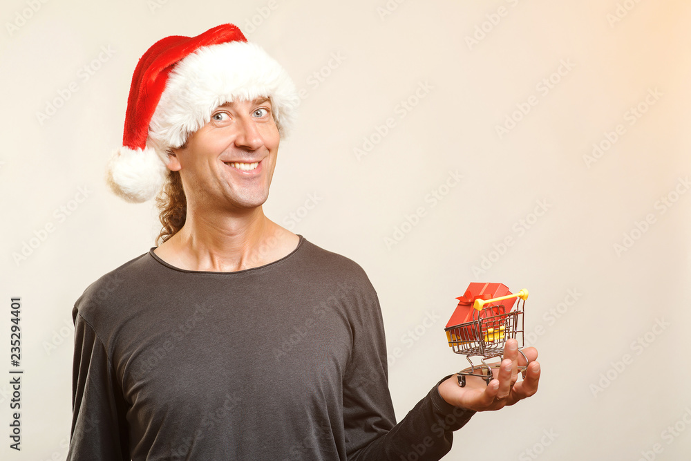 Christmas man with shopping cart, isolated. Christmas gift in cart. Christmas sales and shopping concept. Copy space. Merry Christmas and Happy New Year. Man shopper in Santa hat. Gift box in cart. Christmas man with shopping cart, isolated. Christmas gift in cart. Christmas sales and shopping concept. Copy space. Merry Christmas and Happy New Year. Man shopper in Santa hat. Gift box in cart.