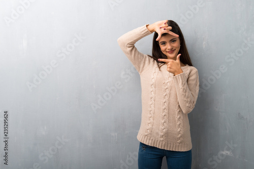 Teenager girl with sweater on a vintage wall focusing face. Framing symbol
