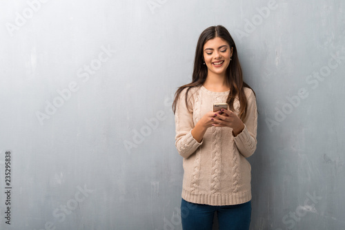 Teenager girl with sweater on a vintage wall sending a message with the mobile