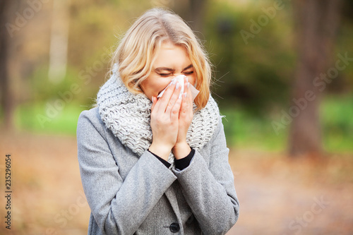 Young woman blowing her nose on the park. Woman portrait outdoor sneezing because cold and flu