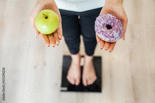 Diet. Woman Measuring Body Weight On Weighing Scale Holding Donut and apple. Sweets Are Unhealthy Junk Food. Dieting, Healthy Eating, Lifestyle. Weight Loss. Obesity