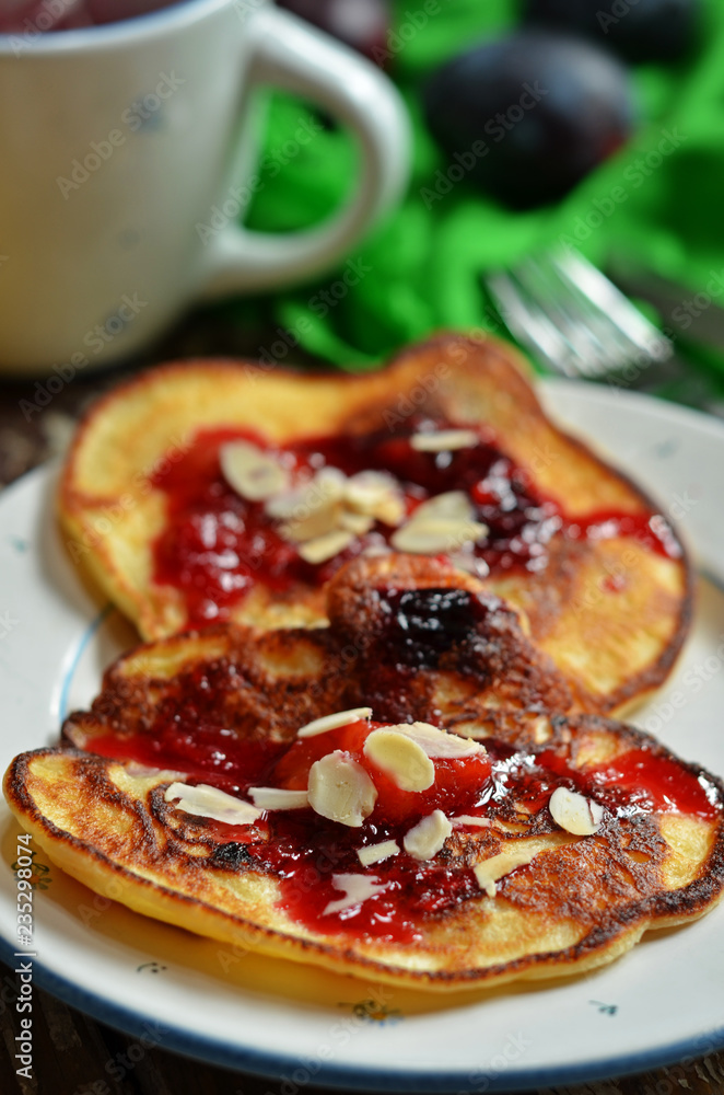 Pancakes with plum jam and almond flakes on a white plate Pancakes with plum jam and almond flakes on a white plate