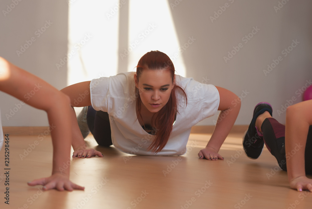 Young focused women doing push ups exercise in fitness class. Group exercise training