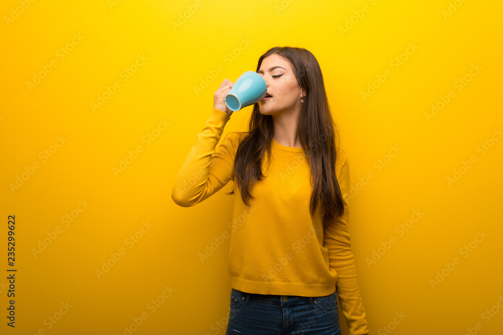 Teenager girl on vibrant yellow background holding a hot cup of coffee Teenager girl on vibrant yellow background holding a hot cup of coffee
