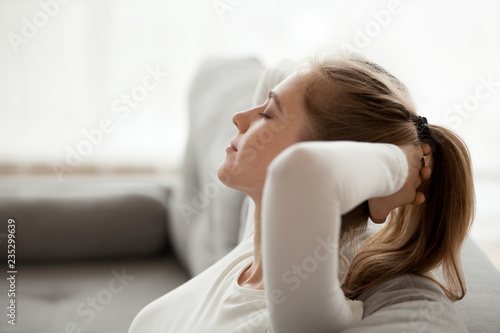Close up of calm young female relax on cozy couch with eyes closed, peaceful girl lying on sofa hands over head having rest at home, dreamy woman stretching enjoying weekend morning in apartment