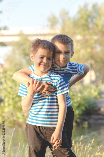 Obraz na plátně Two boys of three years in white T-shirts, jeans and caps are sitting on the grass and hugging