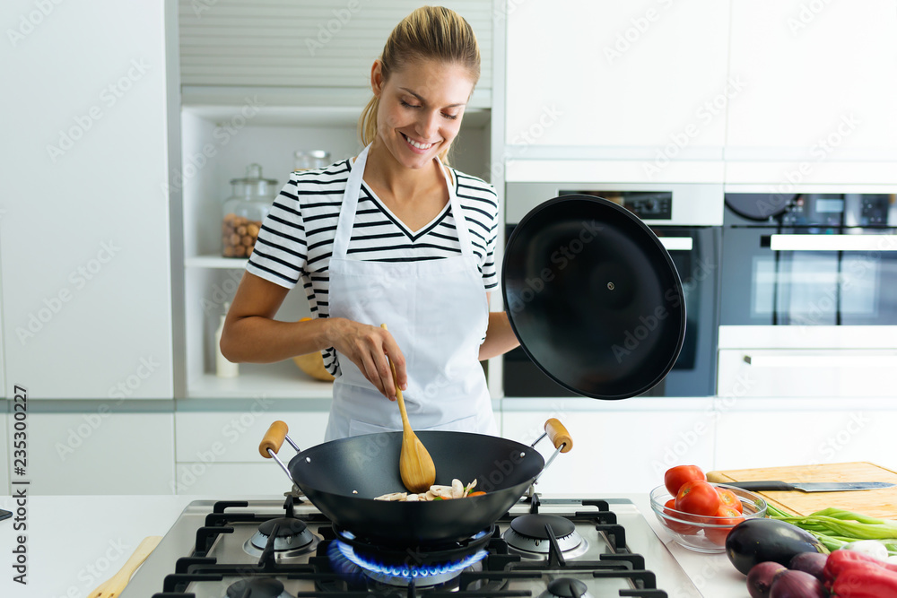 Φωτογραφία Healthy young woman cooking and mixing food in frying pan in the kitchen at home