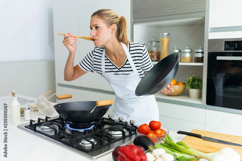 Φωτογραφία Healthy young woman cooking and tasting food with wooden spoon in the kitchen at home