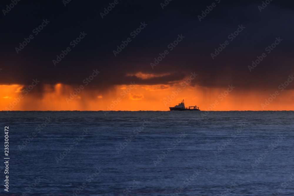 baltic sea with a ship at the horizon. dramatic clouds can be seen on the horizon to the sunrise. weather phenomenon