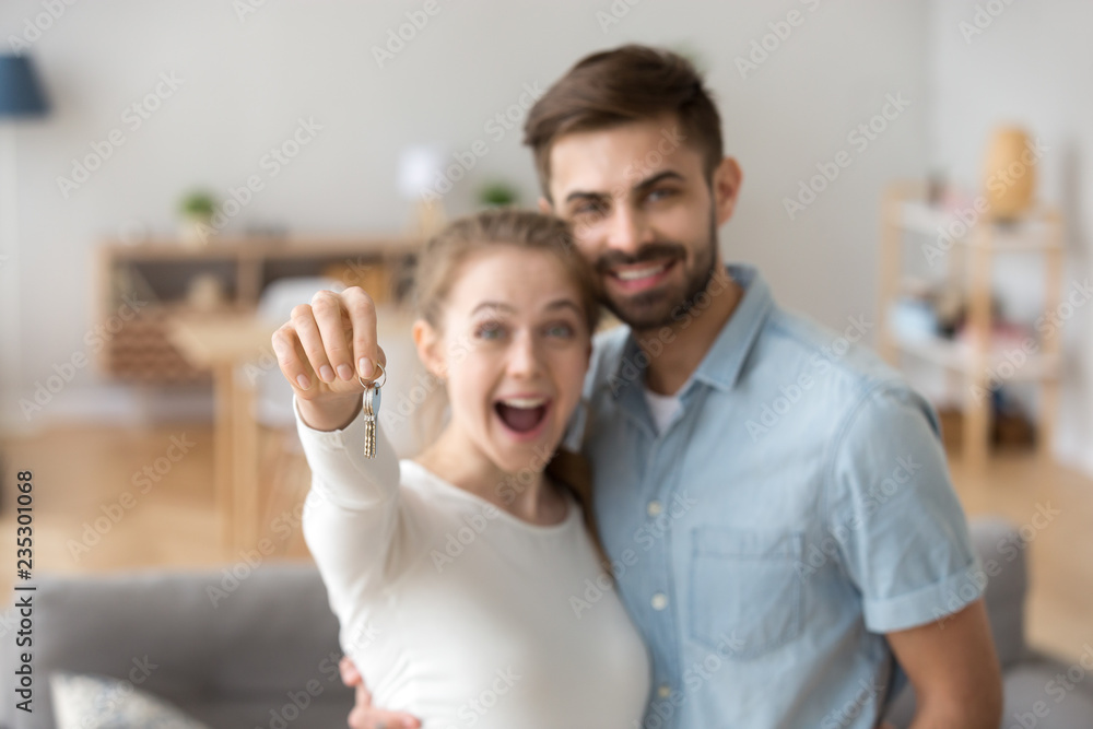 Portrait of happy millennial couple hug holding key to own apartment, young husband and wife excited to buy first home together, smiling married man and woman move in shared house. Ownership concept Portrait of happy millennial couple hug holding key to own apartment, young husband and wife excited to buy first home together, smiling married man and woman move in shared house. Ownership concept