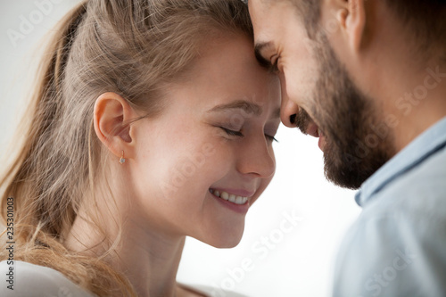Close up of loving man and woman touching forehead having sweet tender moment together, happy millennial couple smile caressing each other, young husband and wife enjoy tenderness at home