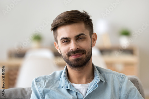 Portrait of happy millennial man looking at camera relaxing at home, headshot of smiling young male posing for picture indoors, confident guy making picture sitting on couch in apartment