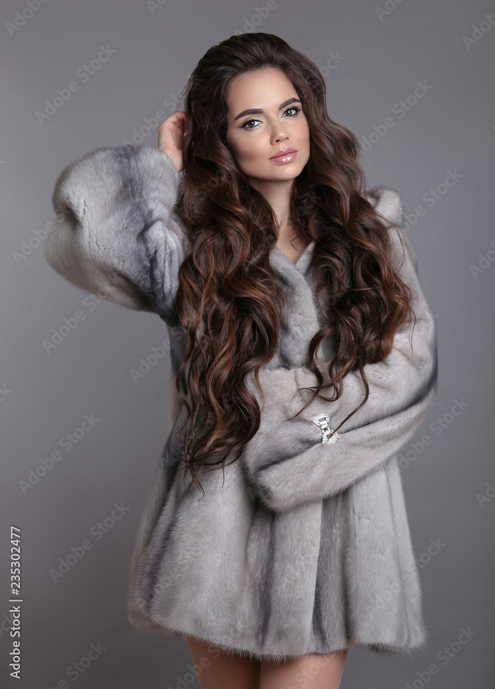 Elegant woman in mink fur coat isolated on gray studio background. Brunette Girl in Luxury Winter outerwear. Elegant woman in mink fur coat isolated on gray studio background. Brunette Girl in Luxury Winter outerwear.