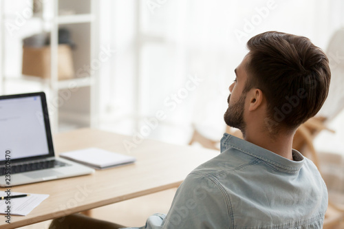 Back view of exhausted millennial man sit at workplace falling asleep, tired male worker distracted from work taking break or nap near laptop, sleepy guy relax with eyes closed sleeping near computer