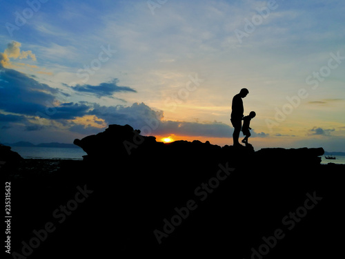 Silhouette of loving father and son walked on seaside and beautiful sunset background.