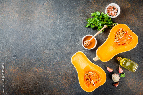 Halves of raw pumpkin or butternut squash, with olive oil, spices and ingredients for cooking on dark background.Top view copy space.