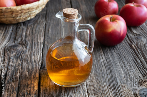 A bottle of apple cider vinegar with apples on a wooden background