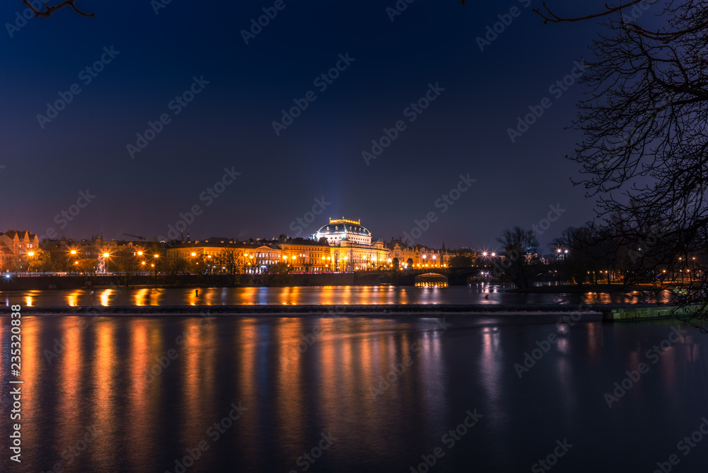 Illuminated classical buildings and street lights reflecting on the Vltava river in Prague before a small waterfall in a cold winter night - 3
