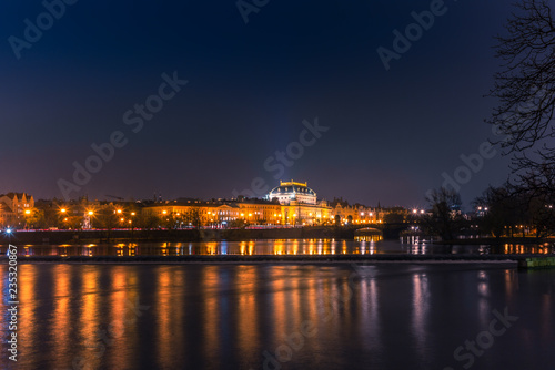 Illuminated classical buildings and street lights reflecting on the Vltava river in Prague before a small waterfall in a cold winter night - 2 © gdefilip