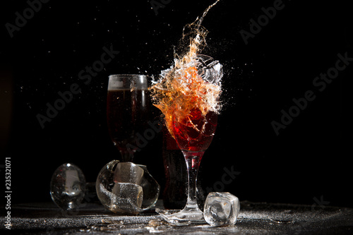 The breaking of a glass with fragments. The explosion of a glass on a black background with a colored liquid. Splashes of colors.