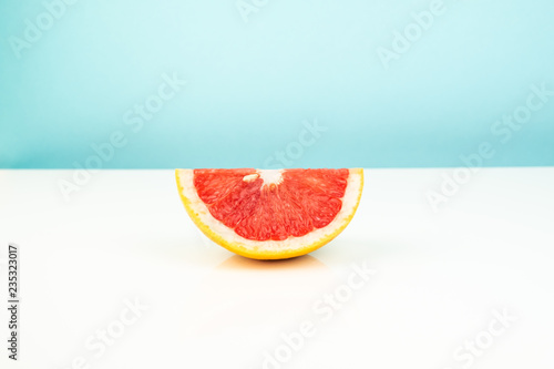 Half of grapefruit on white and blue background. Minimalistic image of slice of citrus at sparse bright environment. photo