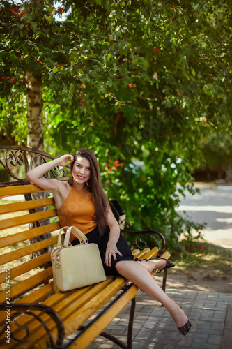 glamorous business girl with bag sits on a bench in the park.