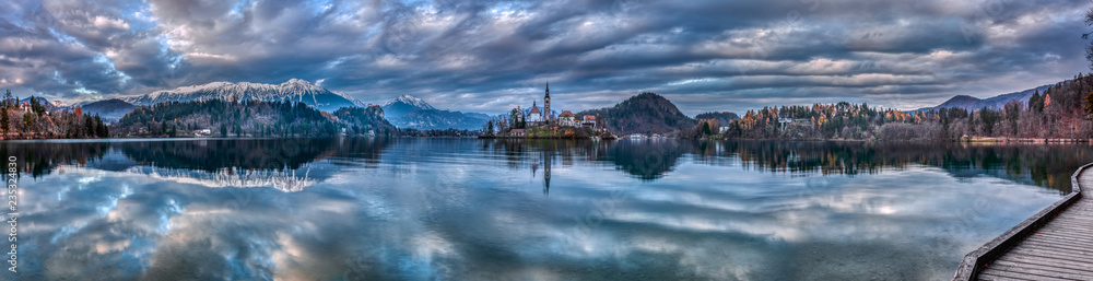 Panoramic shot of the Lake Bled in Slovenia during twilight with the reflection of the surrounding hills and mountains
