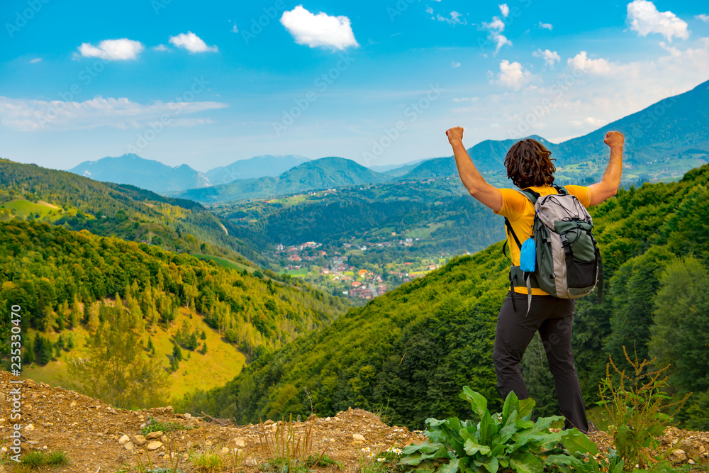 Young mountain hiker with arms raised up, celelbrating and enjoying a beautiful mountain landscape covered with lush forests. Hiking in a sunny summer day. Young mountain hiker with arms raised up, celelbrating and enjoying a beautiful mountain landscape covered with lush forests. Hiking in a sunny summer day.