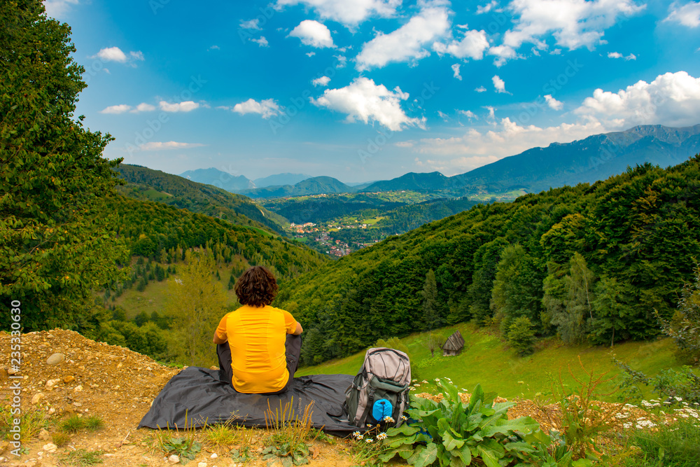 Young mountain hiker sitting on a waterproof nylon blanket in a beautiful mountain landscape and enjoying the view. Hiker concept for summer designs.