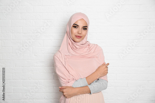 Portrait of young Muslim woman in hijab against brick wall