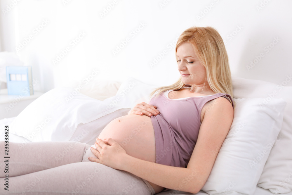 Beautiful pregnant woman resting on bed in light room Beautiful pregnant woman resting on bed in light room