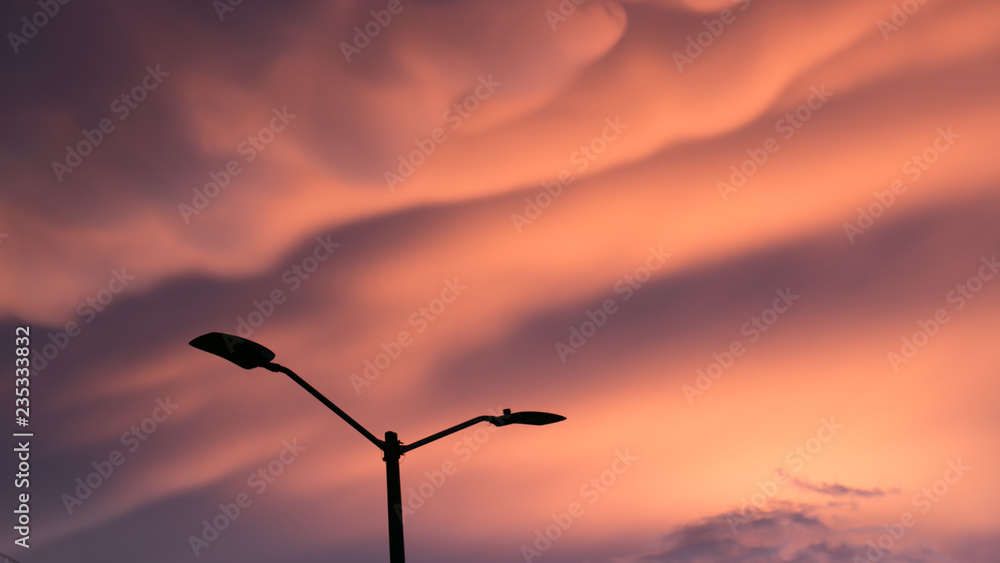 Obraz premium Light post silhouette in front of unbelievable cotton candy cloud sunset in the city