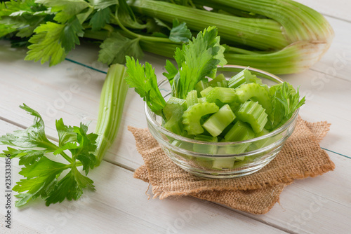 Fresh celery sliced in bowl with bunch celery on white wood background. photo