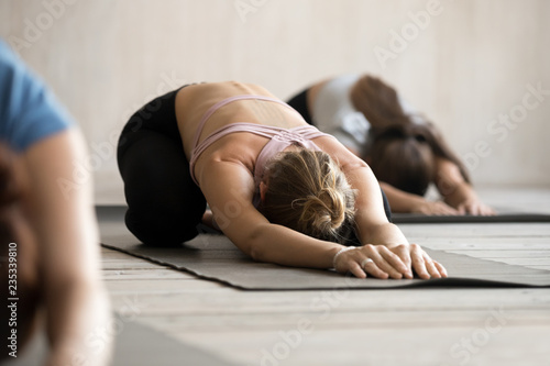 Group of young sporty people practicing yoga lesson, doing Child exercise, Balasana pose, working out, indoor close up, female students training at club, yoga studio. Well being, fitness concept photo