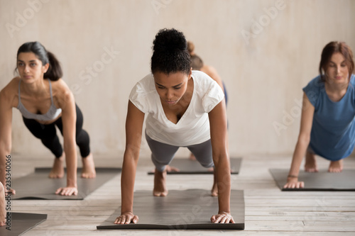 Group of diverse young sporty people doing yoga Plank pose, Push ups or press ups exercise, working out indoor, mixed race students training at sport club or studio. Well being, fitness concept
